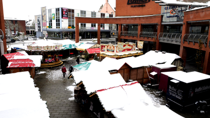 Auf dem Mühlenplatz in Solingen stehen einige Holzhütten und ein Kinderkarussell mit Schnee auf den Dächern