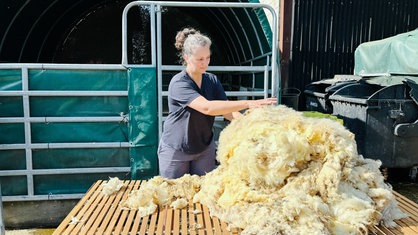 Eine Frau mit grauen Haaren verarbeitet einen Bausch Wolle.