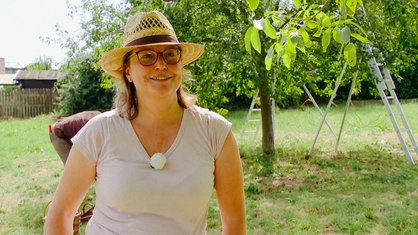 Eine Frau mit Brille, rosa Tshirt und Hut lacht 