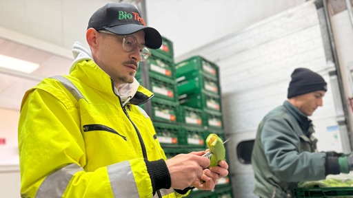 Ben Cikirikci schneidet eine grüne, unreife Banane mit einem Messer der Länge nach auf