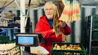 Ein Mann in einer roten Jacke an einem Gemüsestand, er ist dabei, Champignons abzuwiegen