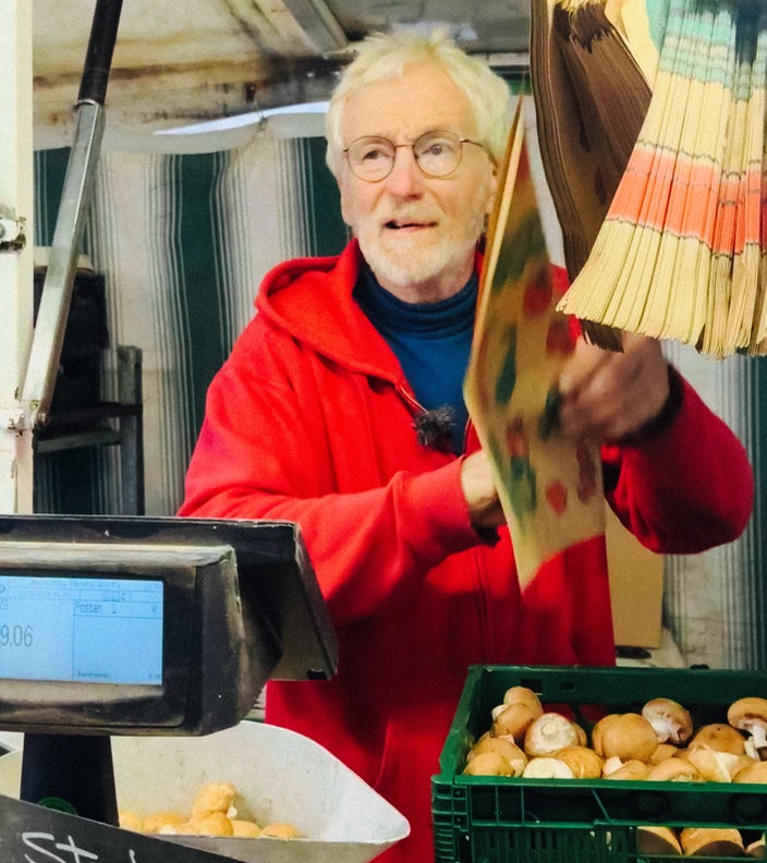 Ein Mann in einer roten Jacke an einem Gemüsestand, er ist dabei, Champignons abzuwiegen