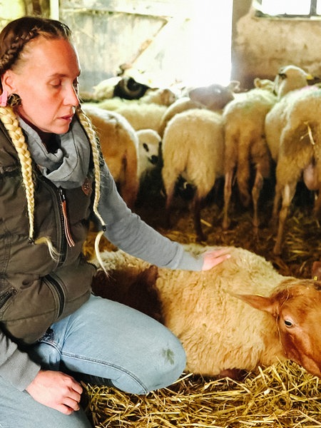 Vicky Diemel sitzt auf dem Boden ihres Schafstalles. Mit der linken Hand streichelt sie ein Schaf, dass neben ihr liegt.