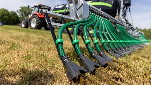 Ein Traktor mit einem Gülletank fährt über ein Feld, durch grüne Schläuche verteilt er die Gülle