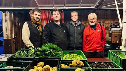 Hinter dem Marktstand mit verschiedenem Gemüse stehen der ältere Landwirt Reinhard Schmidt-Etzold und seine drei Nachfolger.