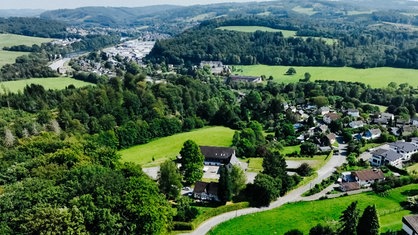 Lufaufnahme einer ländlichen Gegend mit Wald, Wiesen und Häusern.