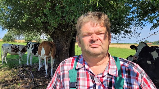 Ein Mann in Arbeitskleidung steht umgeben von Kühen unter einem Baum