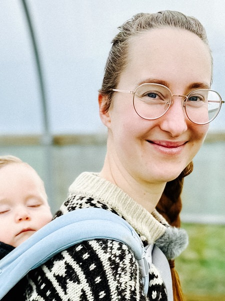 Landwirtin Marie Woeste aus Lüdenscheid steht in einem Folientunnel, sie hat ihren kleinen Sohn in einer Trage auf dem Rücken