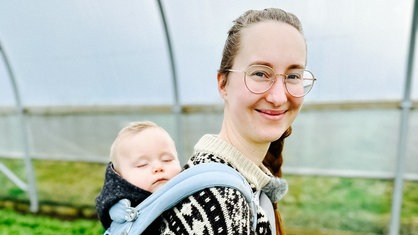 Landwirtin Marie Woeste aus Lüdenscheid steht in einem Folientunnel, sie hat ihren kleinen Sohn in einer Trage auf dem Rücken