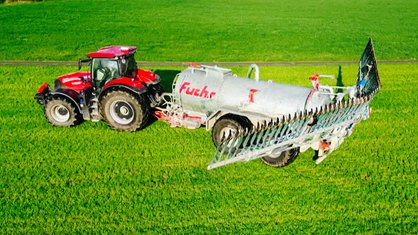 Ein roter Traktor mit einem angehängten Güllewagen fährt über ein Feld