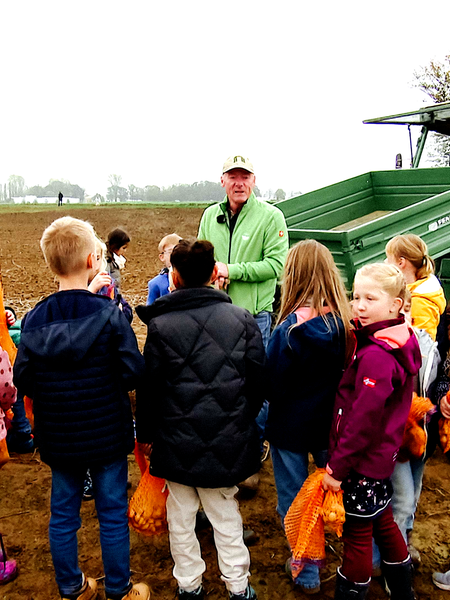 Bern Kockerols steht mit Grundschulkindern auf einem Acker. Hinter ihm sieht man einen Traktor.