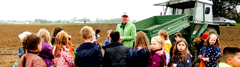 Bern Kockerols steht mit Grundschulkindern auf einem Acker. Hinter ihm sieht man einen Traktor.