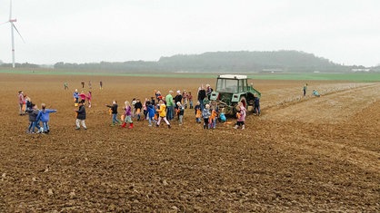 Viele Kinder stehen auf einem Acker. Die meisten Kinder sammeln sich um einen Traktor.