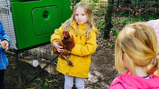 Ein Mädchen mit gelber Jacke hält ein Huhn auf dem Arm.