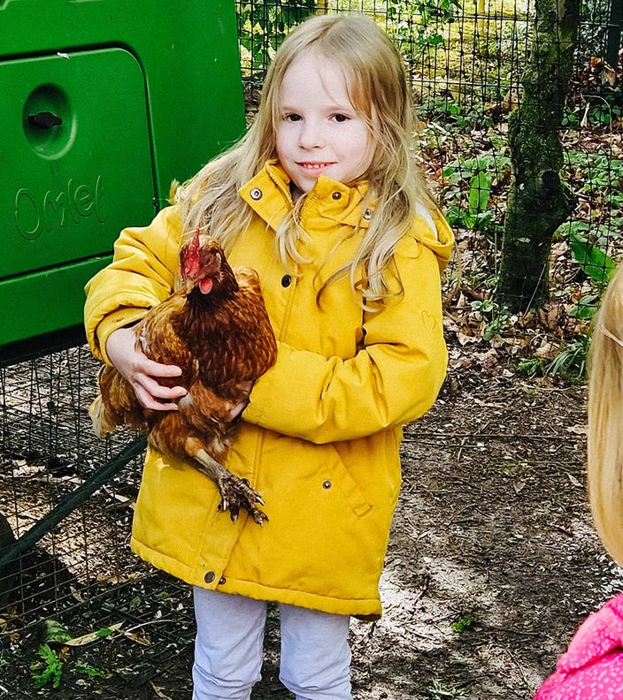 Ein Mädchen mit gelber Jacke hält ein Huhn auf dem Arm.