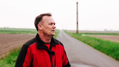 Ein Mann, der eine rote Regenjacke trägt und auf einem Feldweg steht.