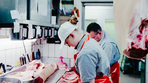 Zwei Menschen in Metzgerschürze an einem Tisch mit Fleischstücken