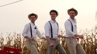 Die drei "Ährenbrüder" Stefan, Henning und Lukas Fockenbrock tanzend auf einem Feld mit weißen Hemden, Hosenträgern und Strohhüten