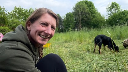 Claudia Lausberg sitzt neben ihren Schafen auf einer Wiese und lächelt in die Kamera