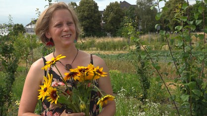 Frau steht in einem Garten und hält einen gelben Blumenstrauß im Arm