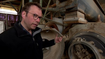 Mann steht vor einer großen Maschine und macht erklärende Geste mit der Hand