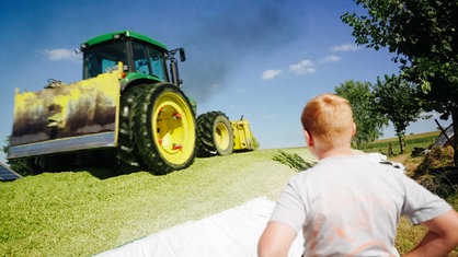 Ein Traktor fährt über ein Maissilo. Im Vordergrund steht ein Junge.