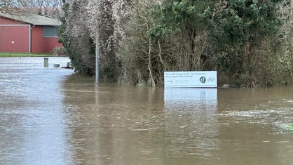 Eine Straße ist überschwemmt. Nur noch ein Schild, ein paar Bäume und ein Haus ragen aus dem Wasser.