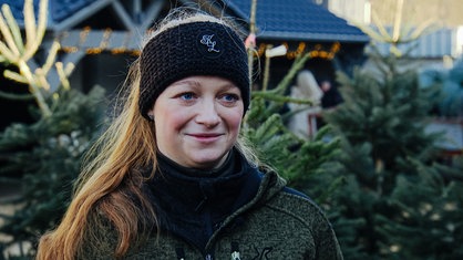 Sarah Neßhöver im Portrait auf dem Hof ihrer Eltern. Im Hintergrund stehen geschlagene Weihnachtsbäume zum Verkauf