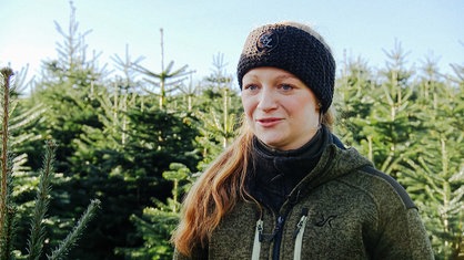 Sarah Neßhöver im Portrait auf einer Baumplantage, im Hintergrund stehen Weihnachtsbäume