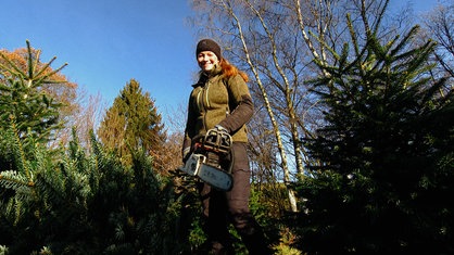 Sarah Neßhöver aus der Froschperspektive in Arbeitskleidung und mit Kettensäge auf der Weihnachtsbaumplantage