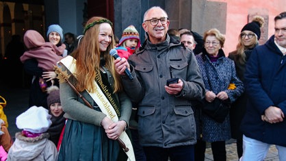 Sarah Neßhöver steht als Weihnachtsbaumkönigin mit dem Bürgermeister von Much vor einer Menschenmenge, er hält ihr ein Mikrofon entgegen 