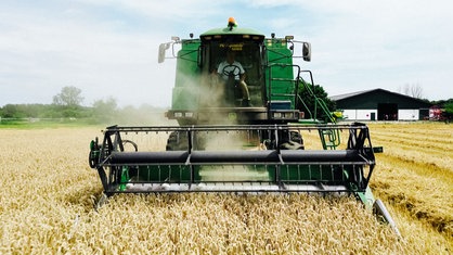 Ein Landwirt sitzt auf einem Mähdrescher und erntet den Weizen auf einem Feld.