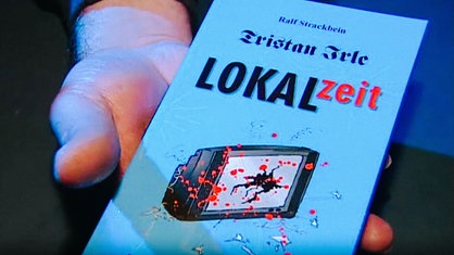 Mann hält den Krimi "Lokalzeit" von Ralf Strackbein in der Hand