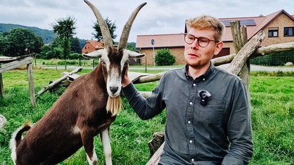 Rechts im Bild Matthis Lemke auf seinem Hof in der halbtotalen, links von ihm eine seiner Ziegen 