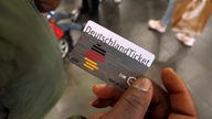 Ein Mensch hält das Deutschland-Ticket in der Hand.