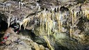 Ein Mann mit Helm und Stirnlampe in einem Durchgang in einer Höhle, von oben ragen viele Tropfsteine ins Bild