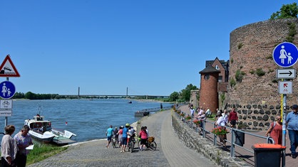 Die historische Stadtmauer und die Uferpromenade in Rees mit zahlreichen Spaziergängern und Fahrradfahrern