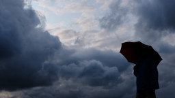 Ein Mann mit einem Regenschirm steht vor dunklen Wolken