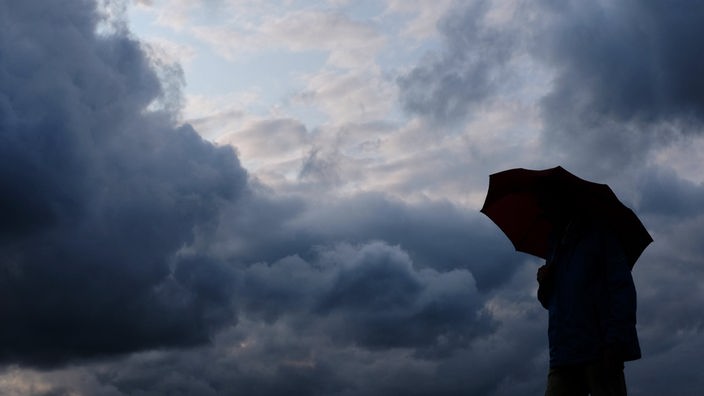 Ein Mann mit einem Regenschirm steht vor dunklen Wolken