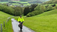 Ein Fahrradfahrer fährt einen Weg, der durch grüne Wiesen führt.