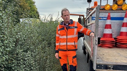 Bernd Vieth steht neben einem Auto auf der Autobahn. Auf dem Auto liegen Verkehrsleitkegel