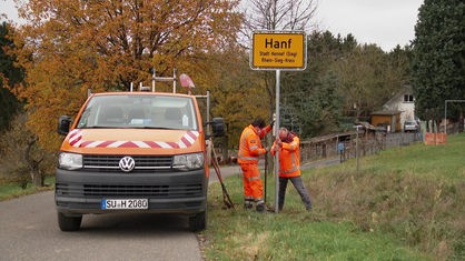 Straßenbauer montieren ein Ortsschild im Ort Hanf