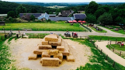 Ein Bauernhof, im Vordergrund ist ein großer Strohhaufen zum Klettern als Spielplatz