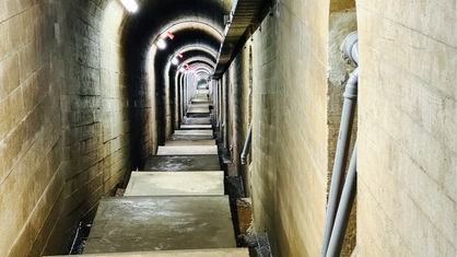 Ein tunnelartiger Gang, in welchem Treppen nach unten führen.