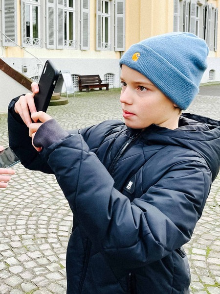 Zwei Jungs stehen mit einem Handy und einem Tablet vor dem Schloss Morsbroich