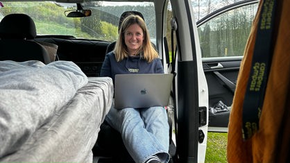Eine Frau sitzt mit einem aufgeklappten Laptop in einem Camper.