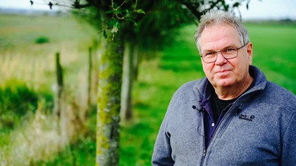 Ein Mann in mittlerem Alter und blauem Pullover schaut in die Kamera