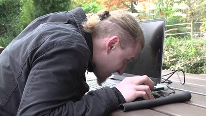 Ein Mann sitzt am Laptop, den Kopf aufgrund seiner Sehbehinderung dabei sehr nah am Bildschrim