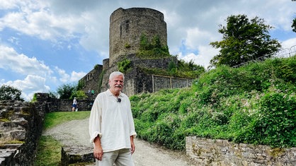 Peter Heinz Krause steht vor dem großen Turm der Burgruine Windeck