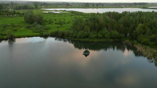 Auf einem See umringt von grünen Wiesen und Bäumen schwimmt ein Floß.